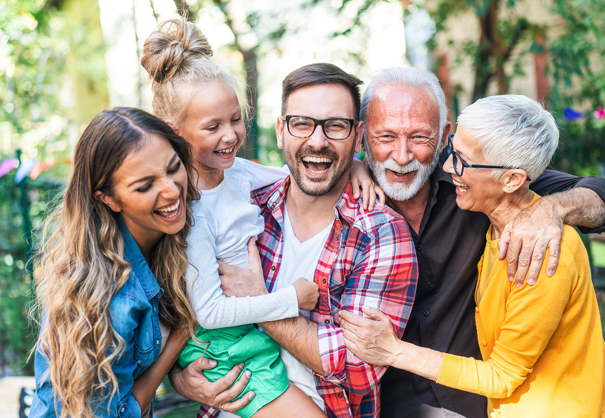 The whole family, including mom, dad, daughter, grandad, and grandma, smiles together in a park, radiating happiness and promoting a healthy, joyful lifestyle.