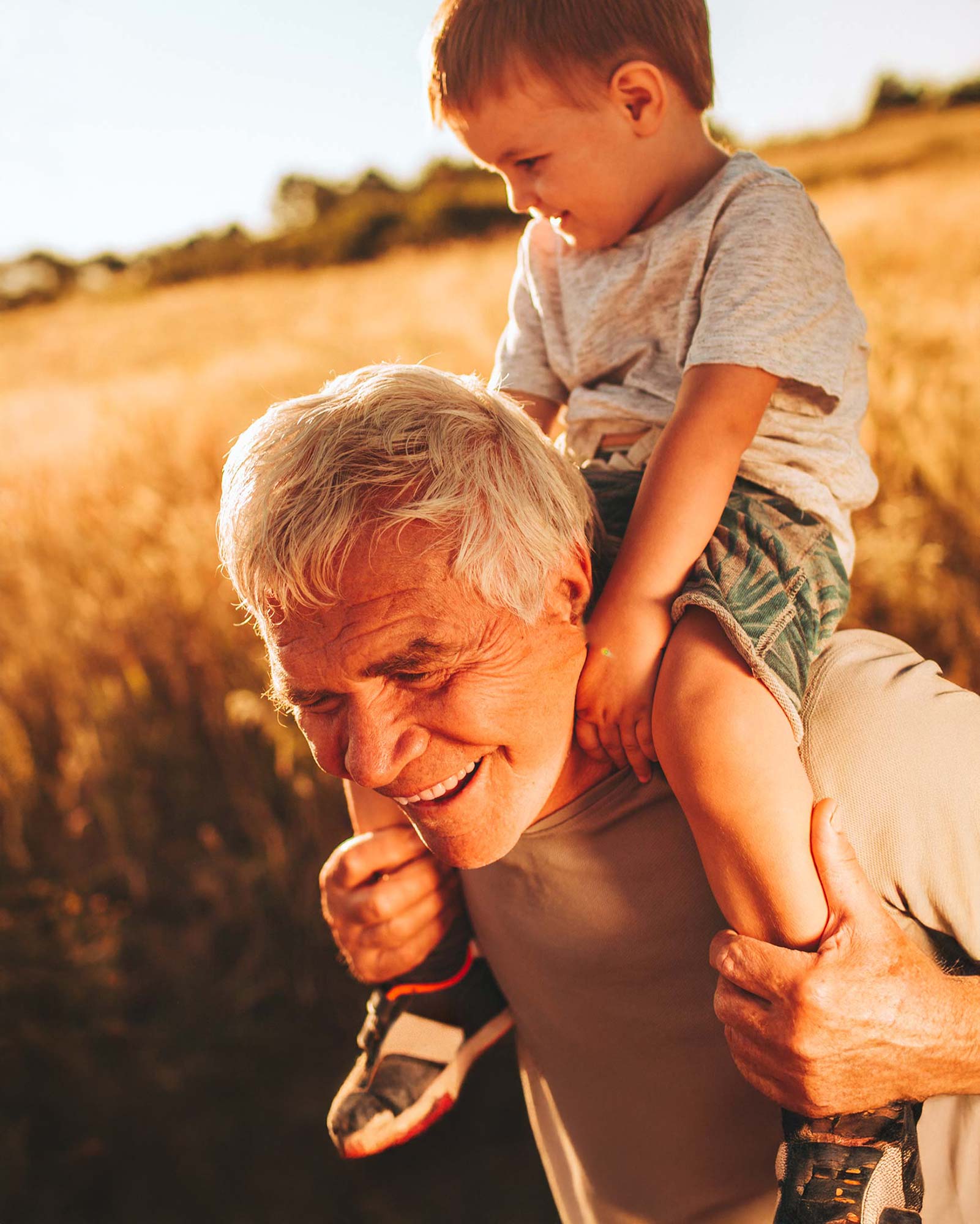 Granddad carries his grandson on his back, both smiling and enjoying a joyful, happy moment together.