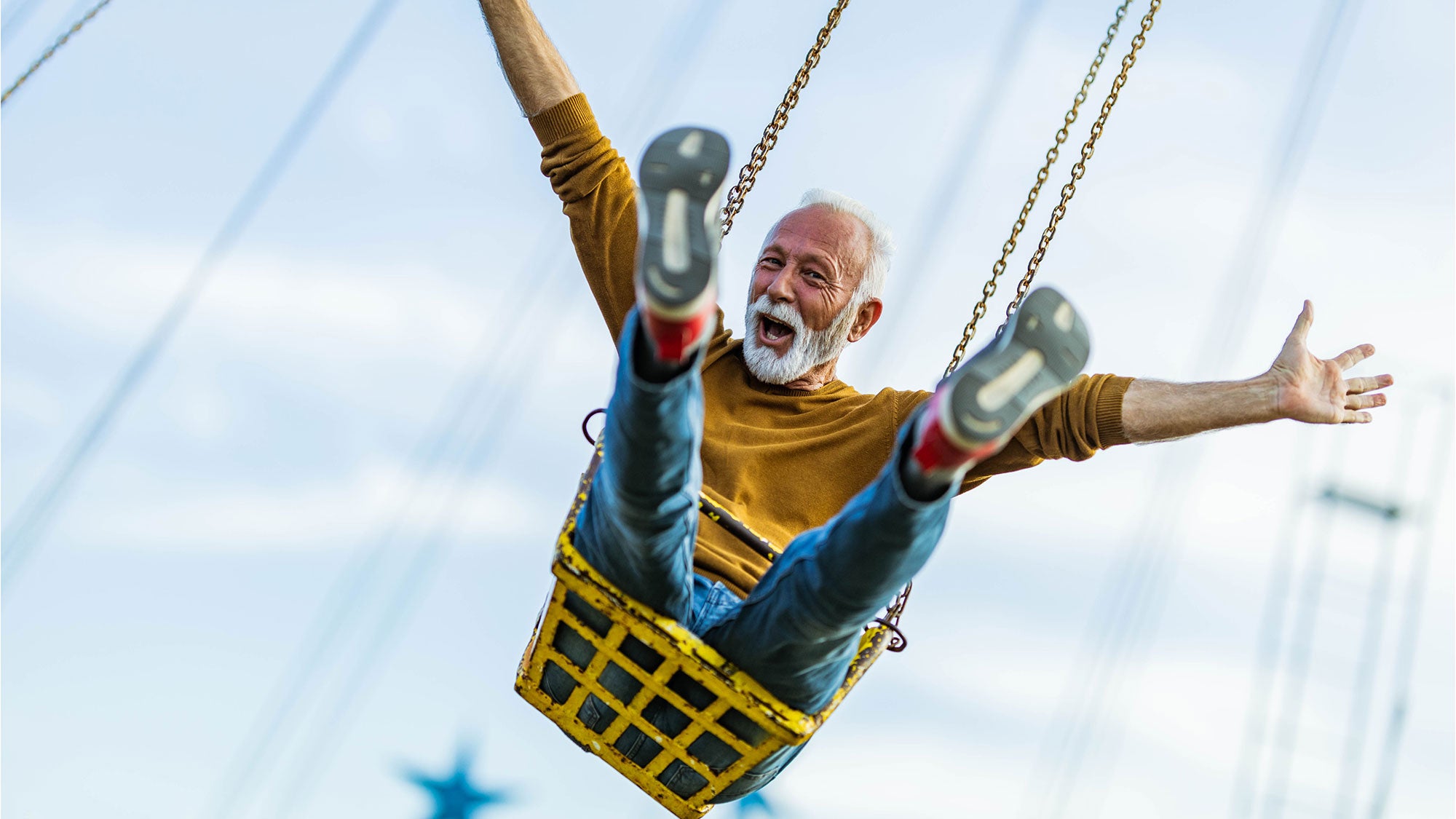 A senior enjoys a fun moment on a flying chair with arms wide open, smiling and having a good time, embracing joy and adventure.