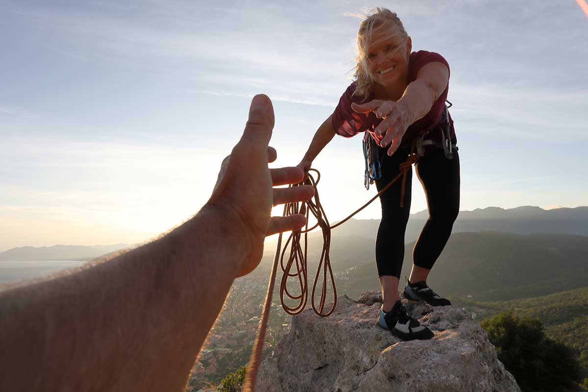 A couple of climbers, happy and smiling woman climber reaching her hand to help her partner reach the top