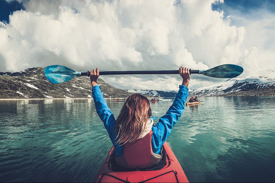 Woman in a kayak celebrates reaching her hands in the air, happy to finish the kayak ride.